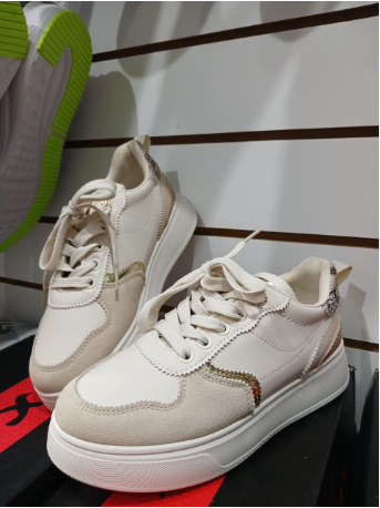 Zapatillas color crema con suela blanca. Se encuentran en una tienda, sobre una caja.