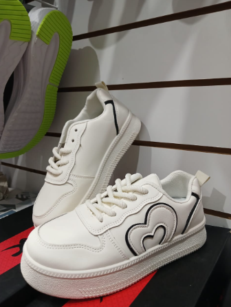 Zapatillas blancas con ribete negro y diseño en forma de corazón, en exhibición en una tienda.
