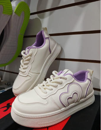 Zapatillas blancas con ribete negro y diseño en forma de corazón, en exhibición en una tienda.