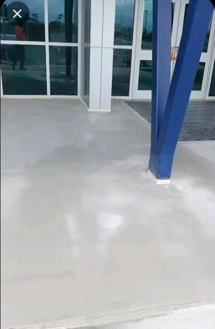 A person is standing in front of a building with a blue pole.