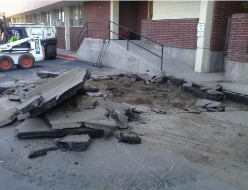 A bobcat is working on a sidewalk in front of a brick building
