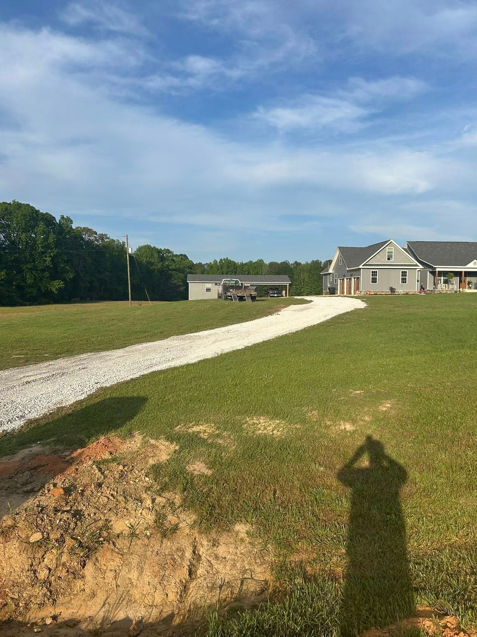 A dirt road leading to a house in the middle of a grassy field.