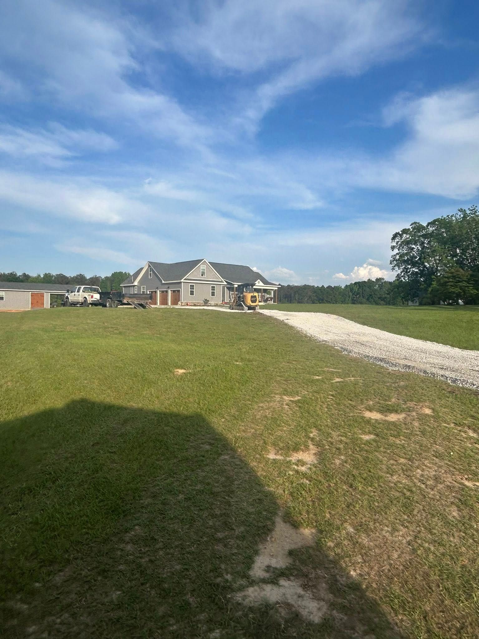 A dirt road leading to a house in the middle of a grassy field.