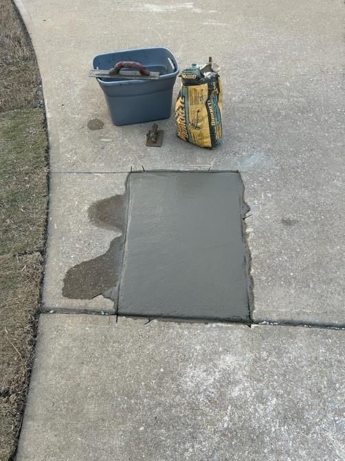A bag of concrete is sitting on a sidewalk next to a bucket.