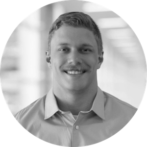 Smiling man with a mustache in a button-down shirt, photographed in grayscale.