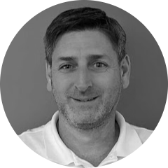 Smiling man with short hair and stubble in a white collared shirt.