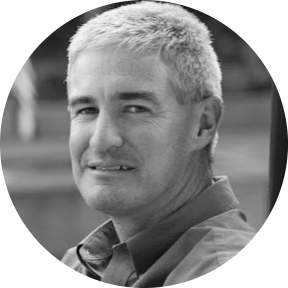 White and black photo of a man with graying hair and a collared shirt, smiling. He appears to be outdoors.