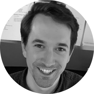 Man with dark hair, smiling in front of a document-filled wall.