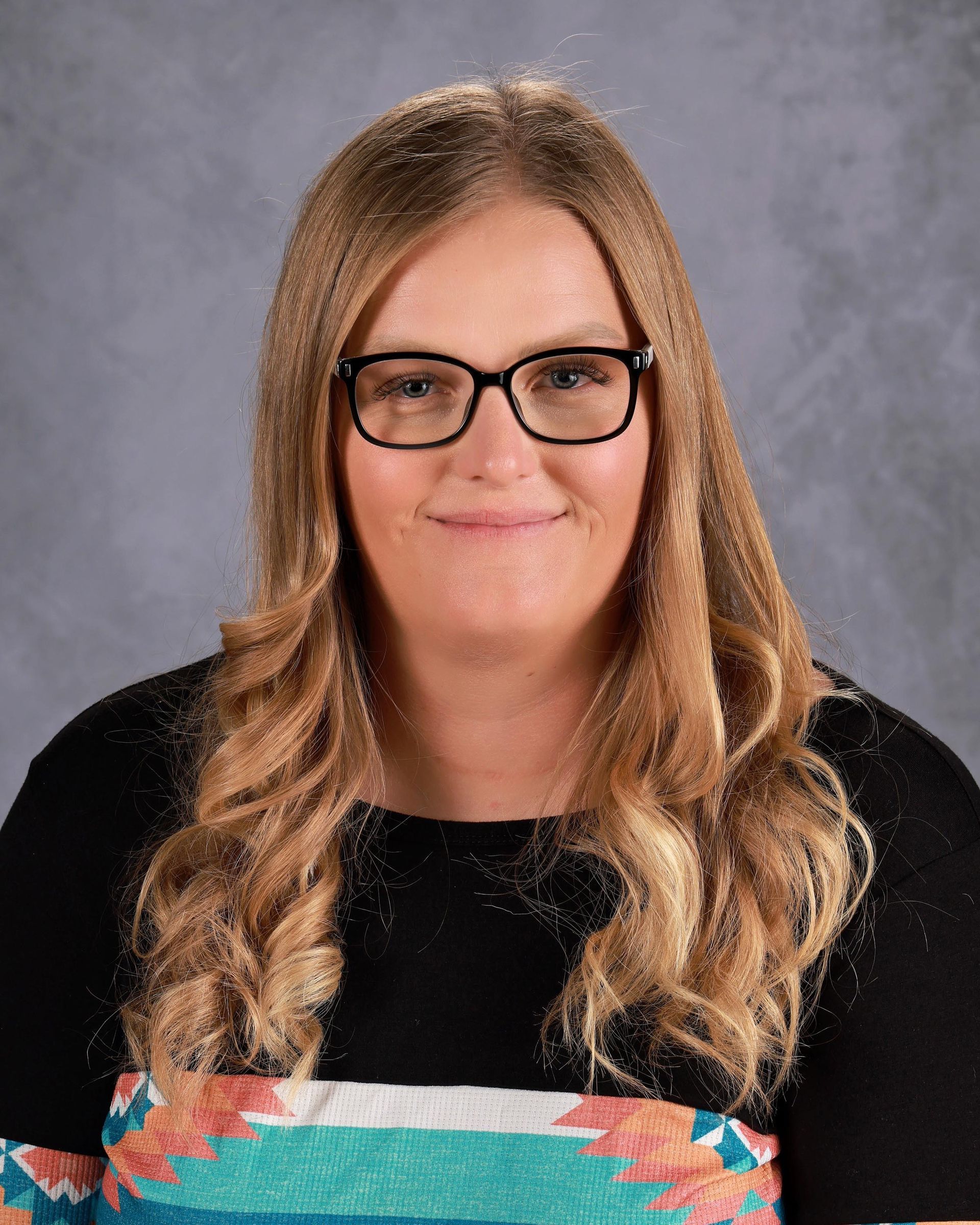 A woman wearing glasses and a blue shirt is smiling for the camera.