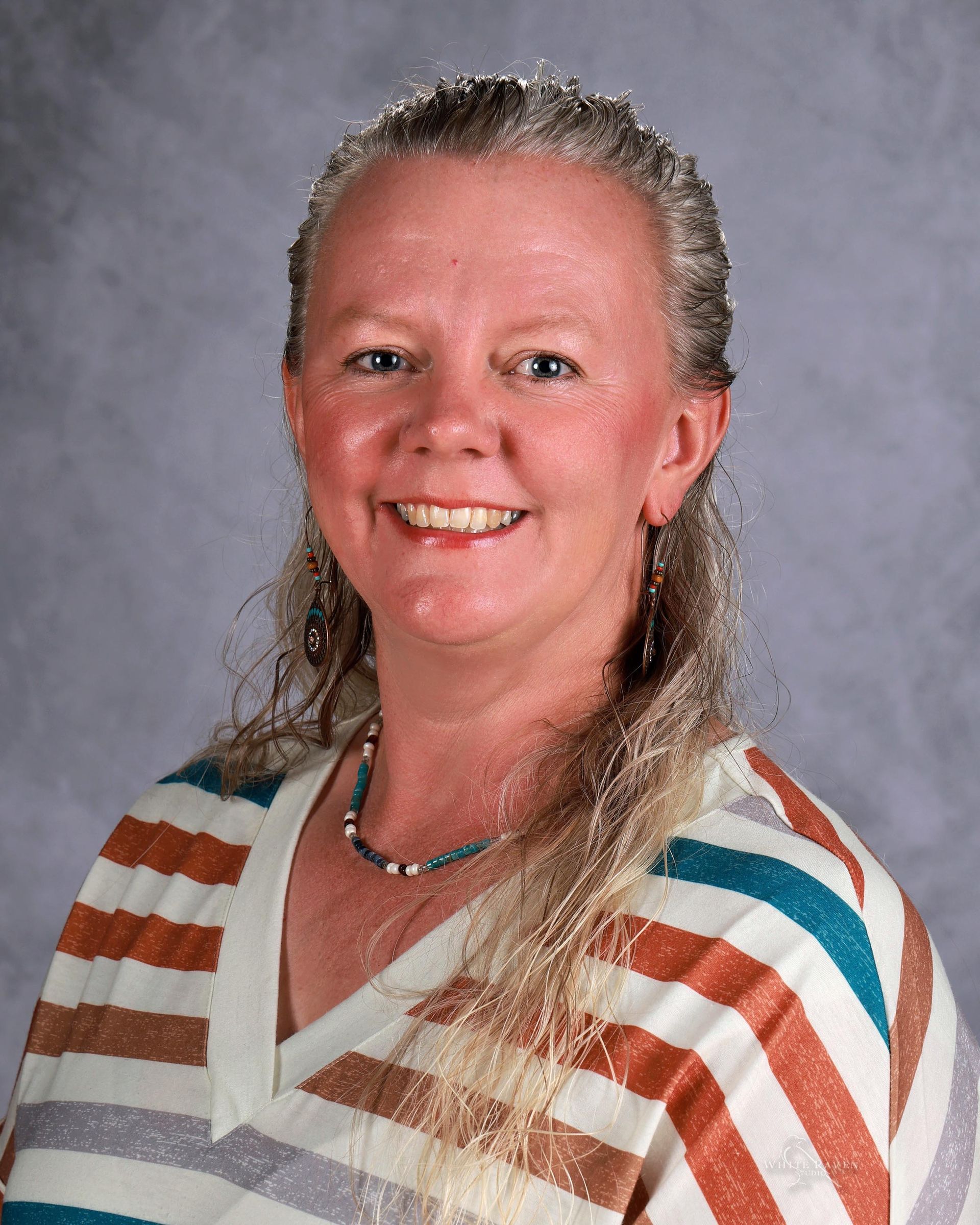 A woman with long blonde hair is smiling and wearing a green shirt.
