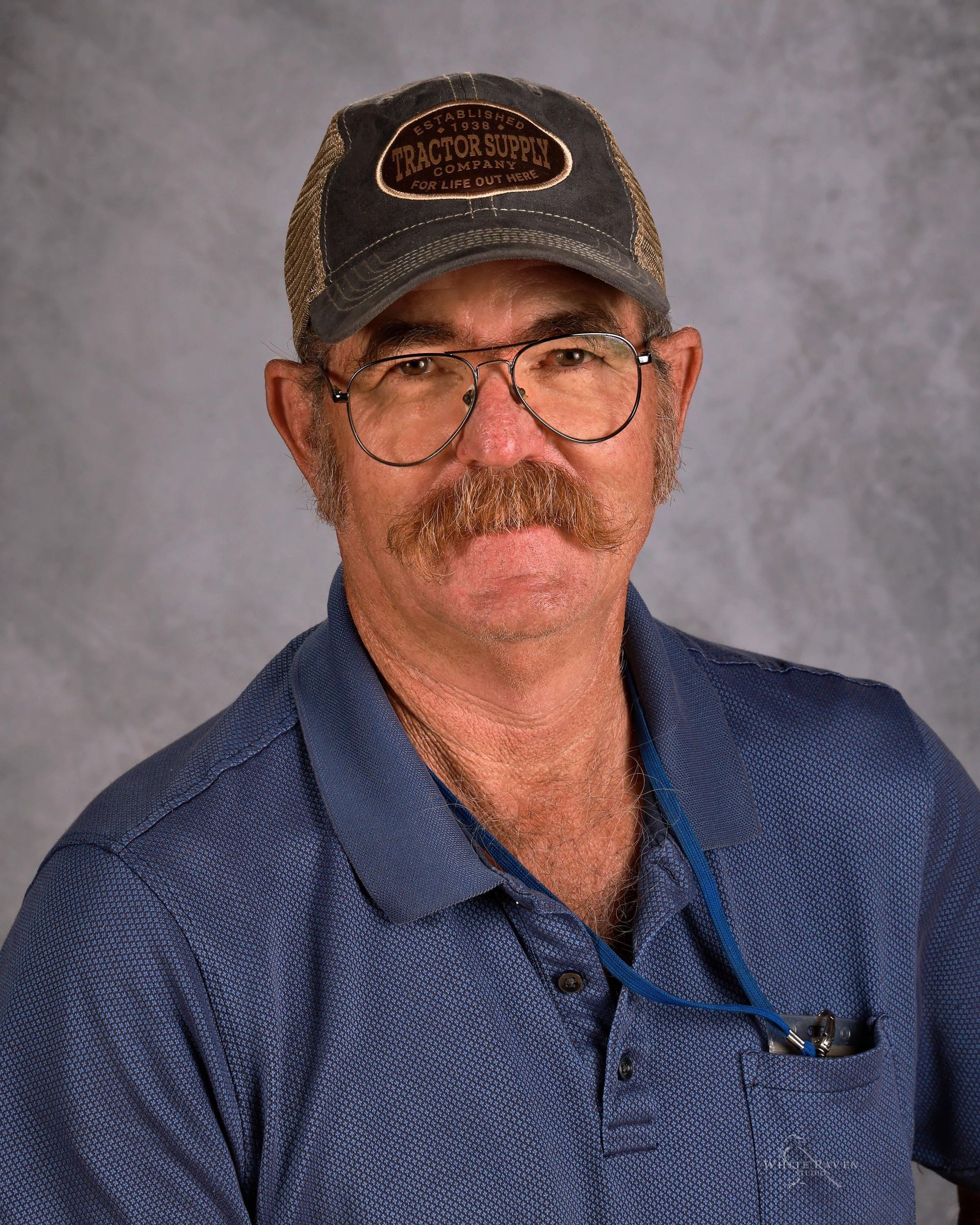A man with a mustache and glasses is wearing a baseball cap and plaid shirt.