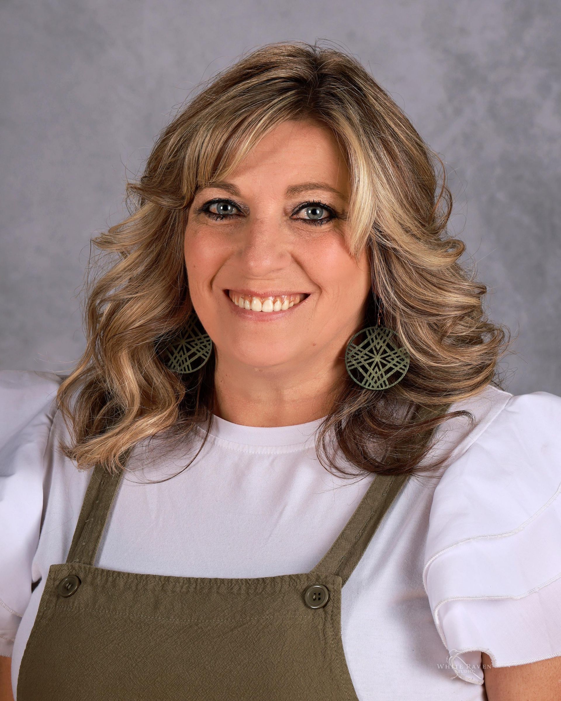 A woman wearing a green necklace and earrings is smiling for the camera.