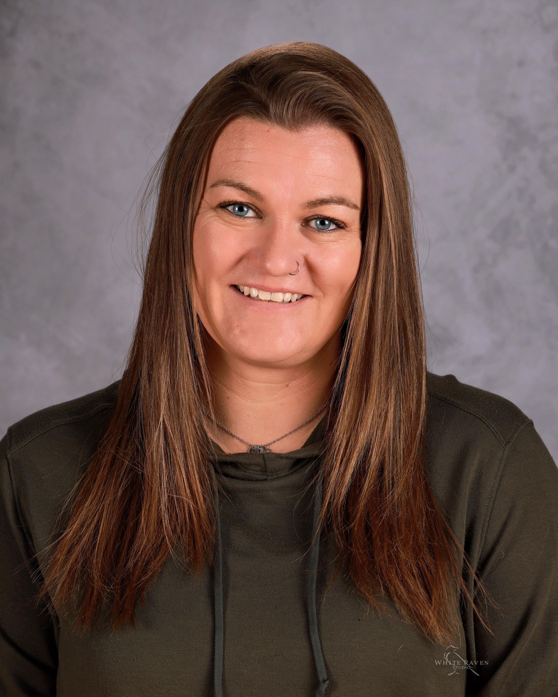 A woman in a pink sweater is smiling in front of a white wooden wall.
