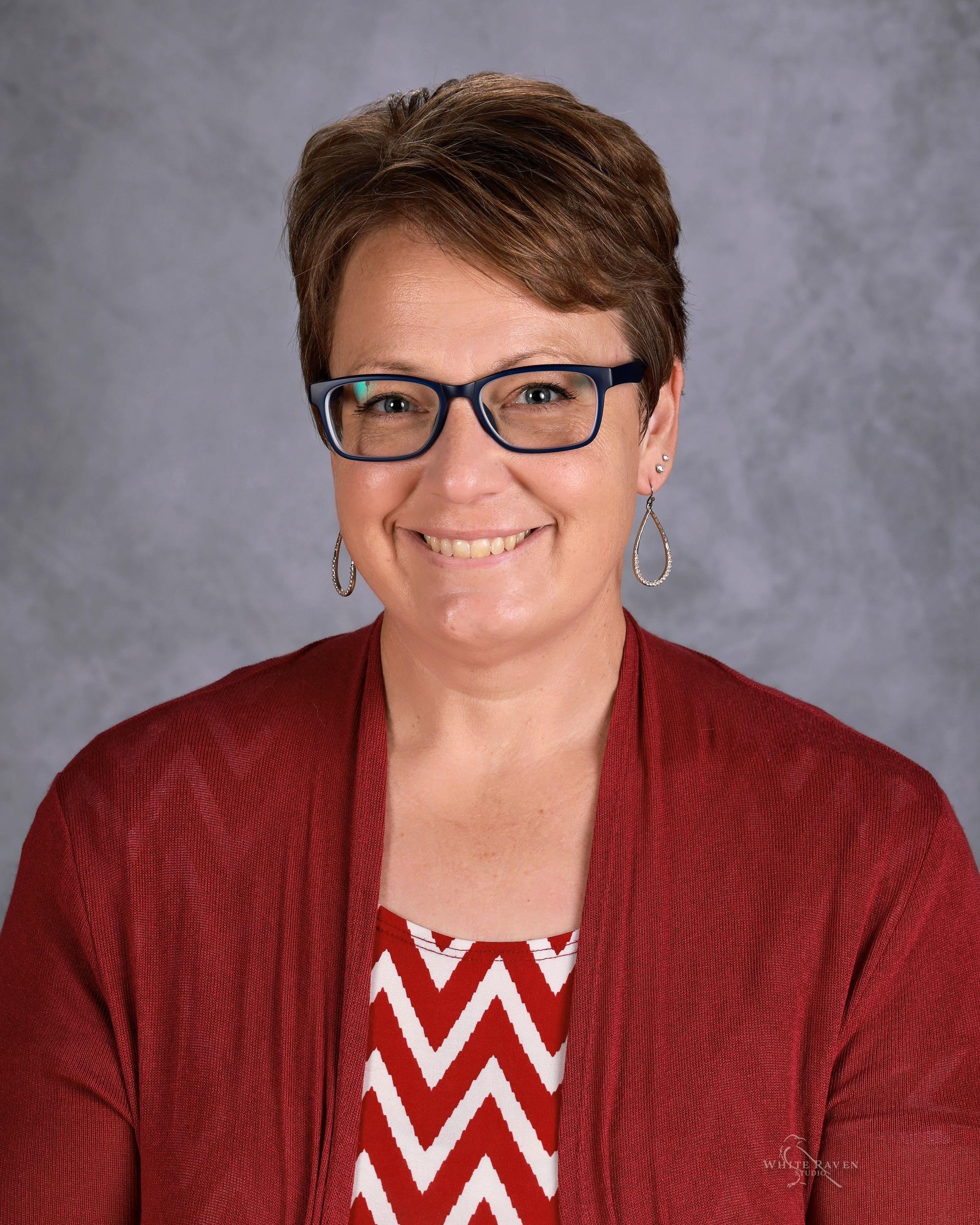 A woman with brown hair and a white shirt is smiling for the camera.
