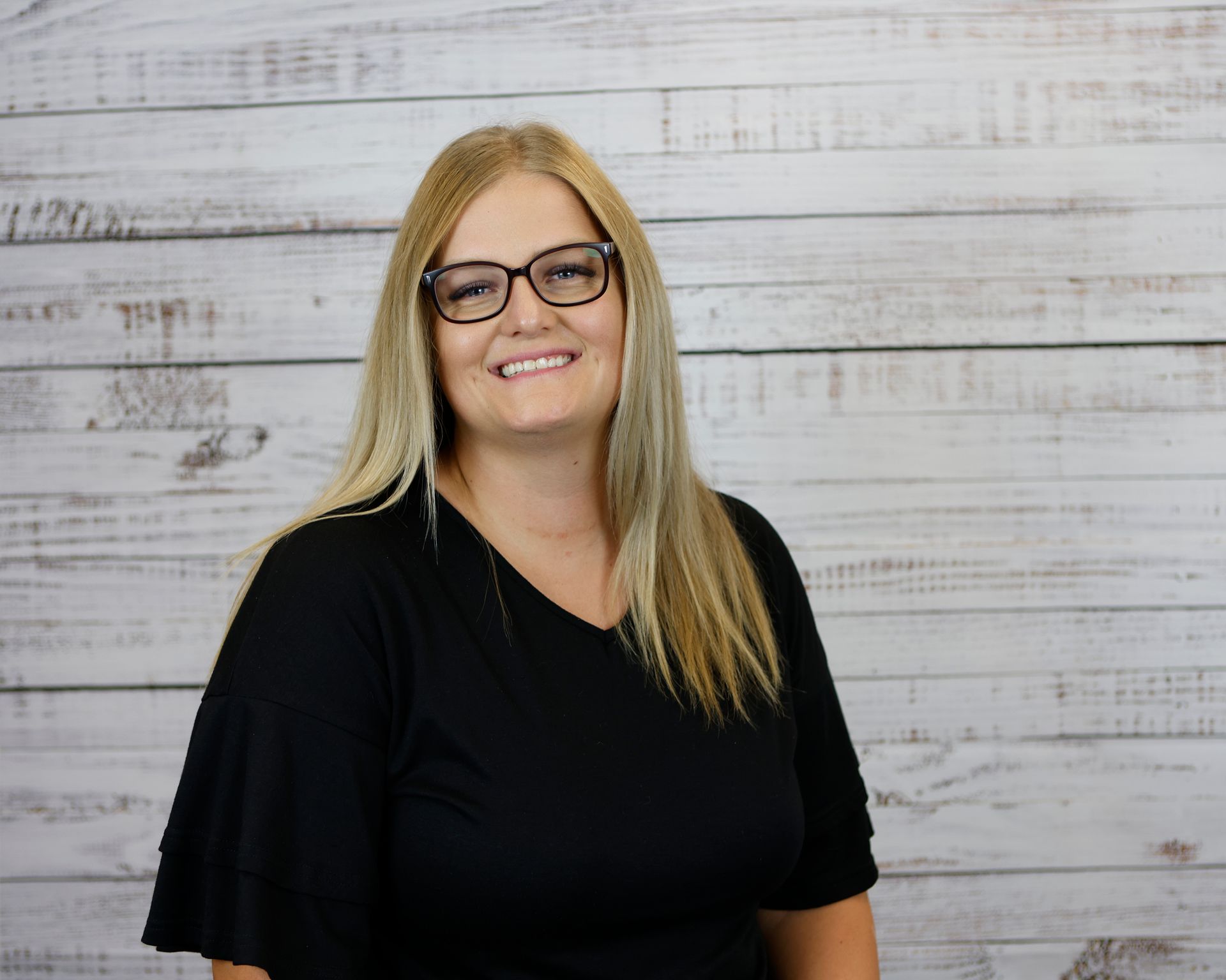 A woman wearing glasses and a blue shirt is smiling for the camera.