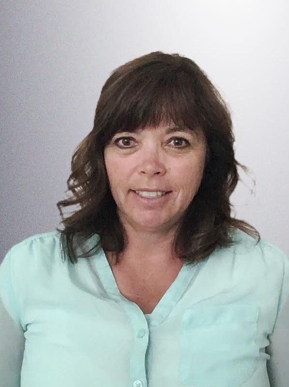 A woman in a blue shirt and cardigan is smiling for the camera.