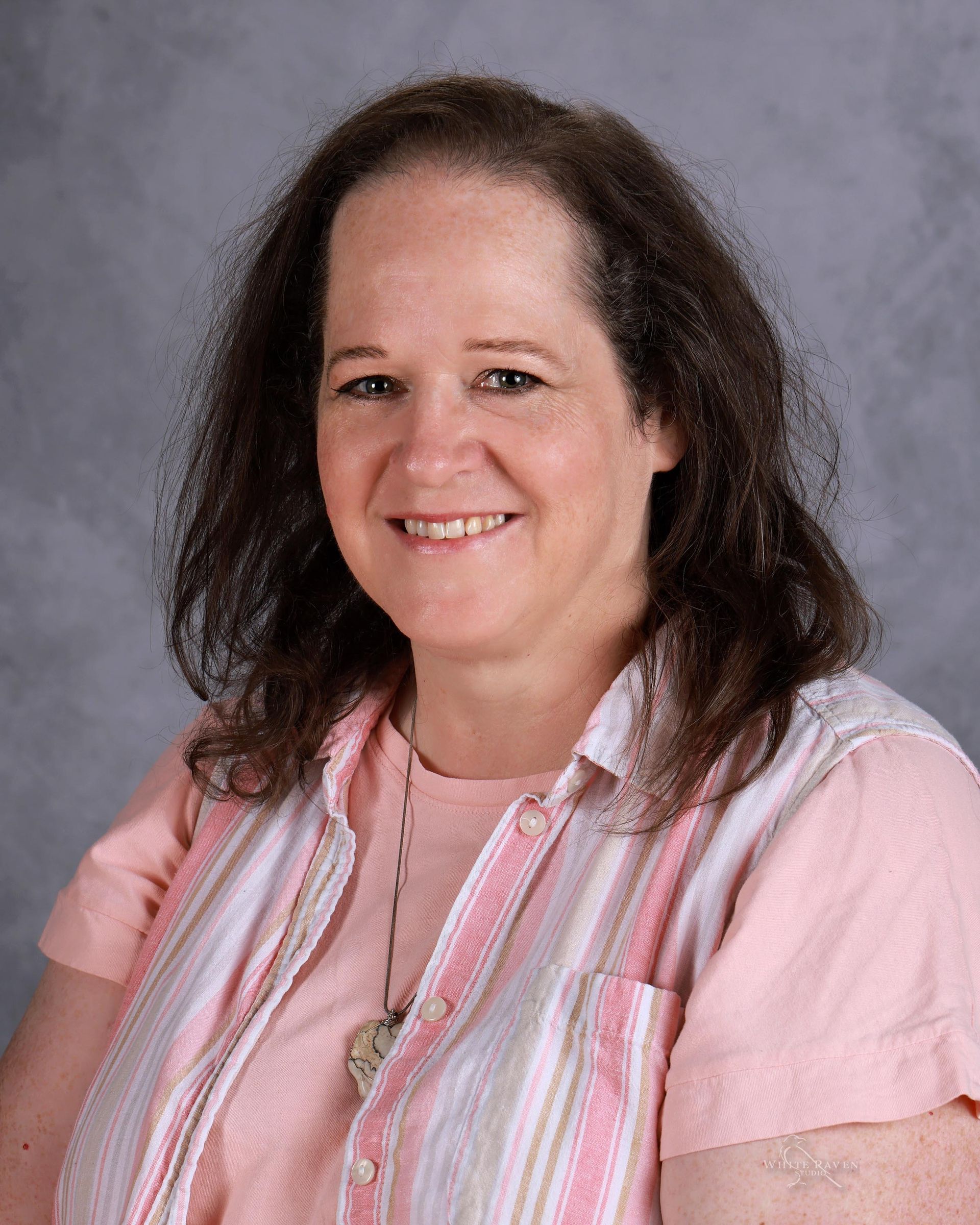 A young woman with blonde hair and a necklace is smiling for a picture.