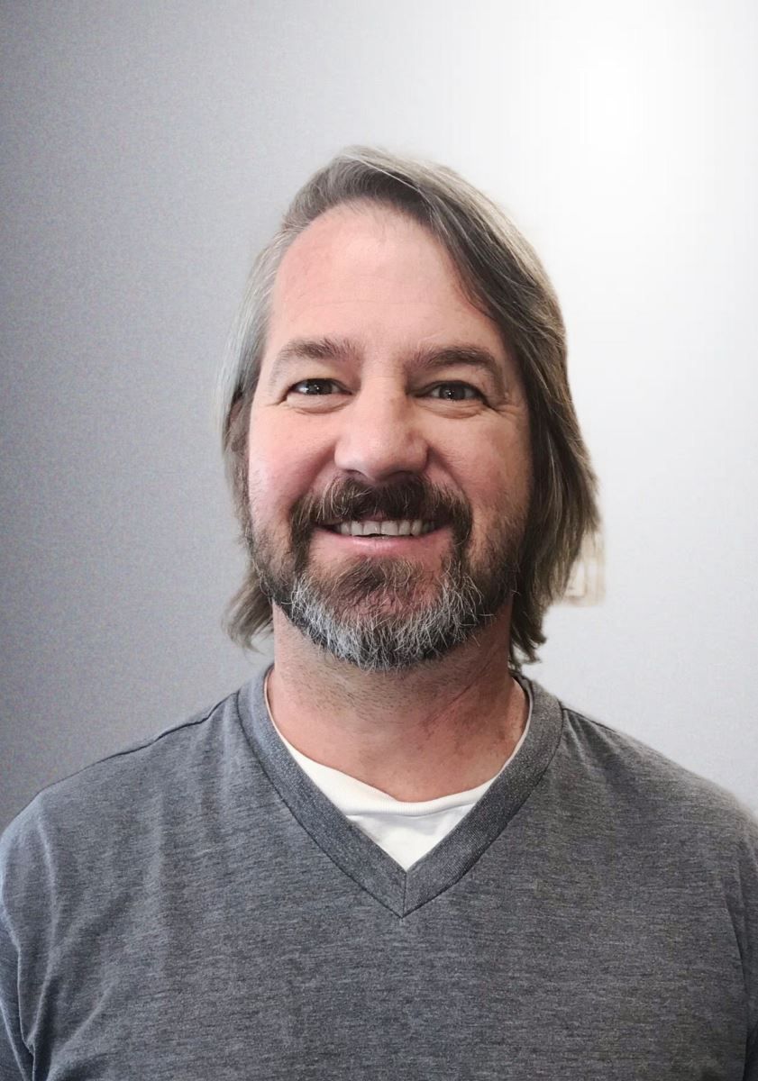 A man with long hair and a beard is smiling for the camera.