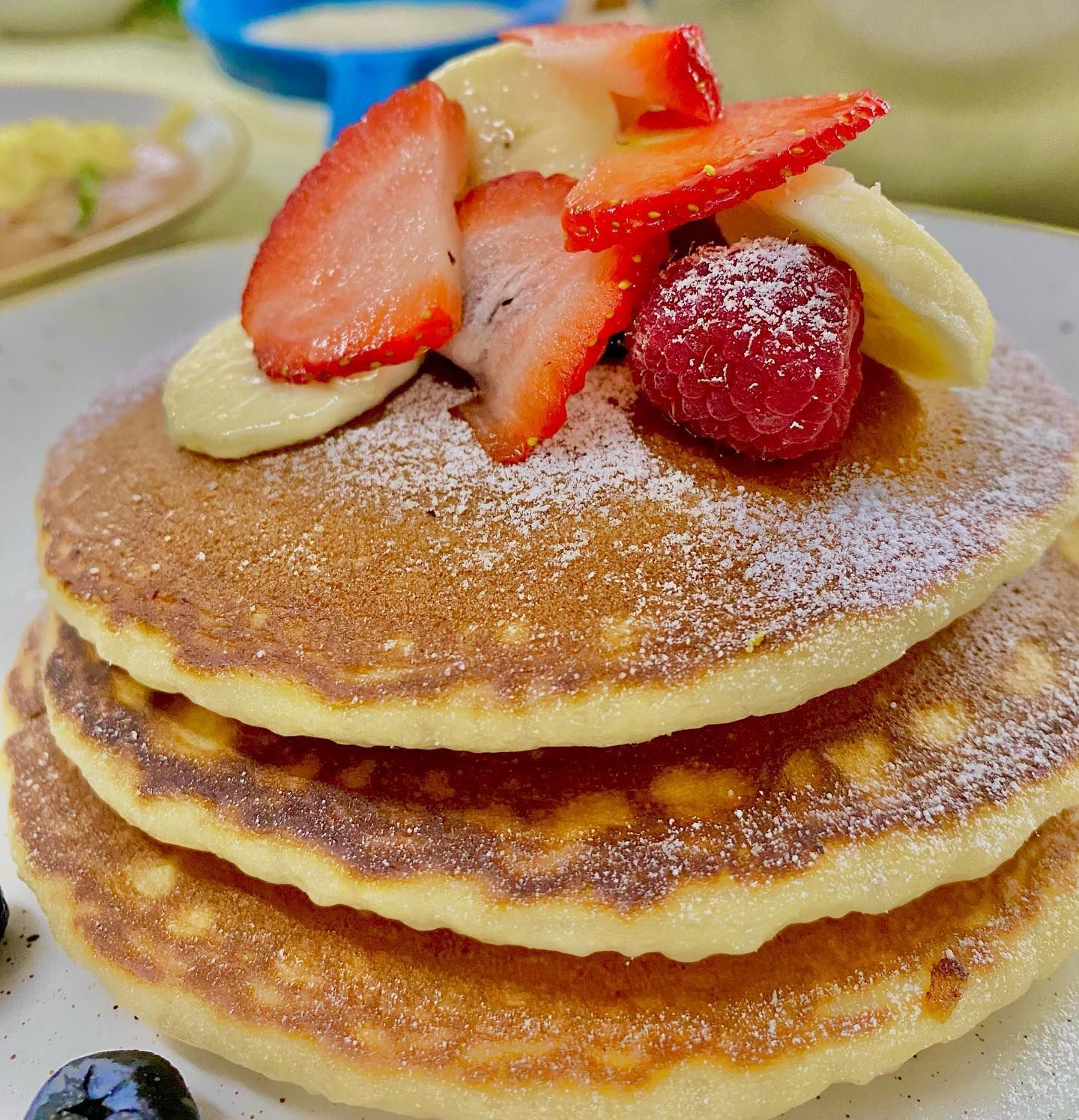 Torre de panqueques cubierta con fruta (fresas, plátano, frambuesa) y espolvoreada con azúcar glas.