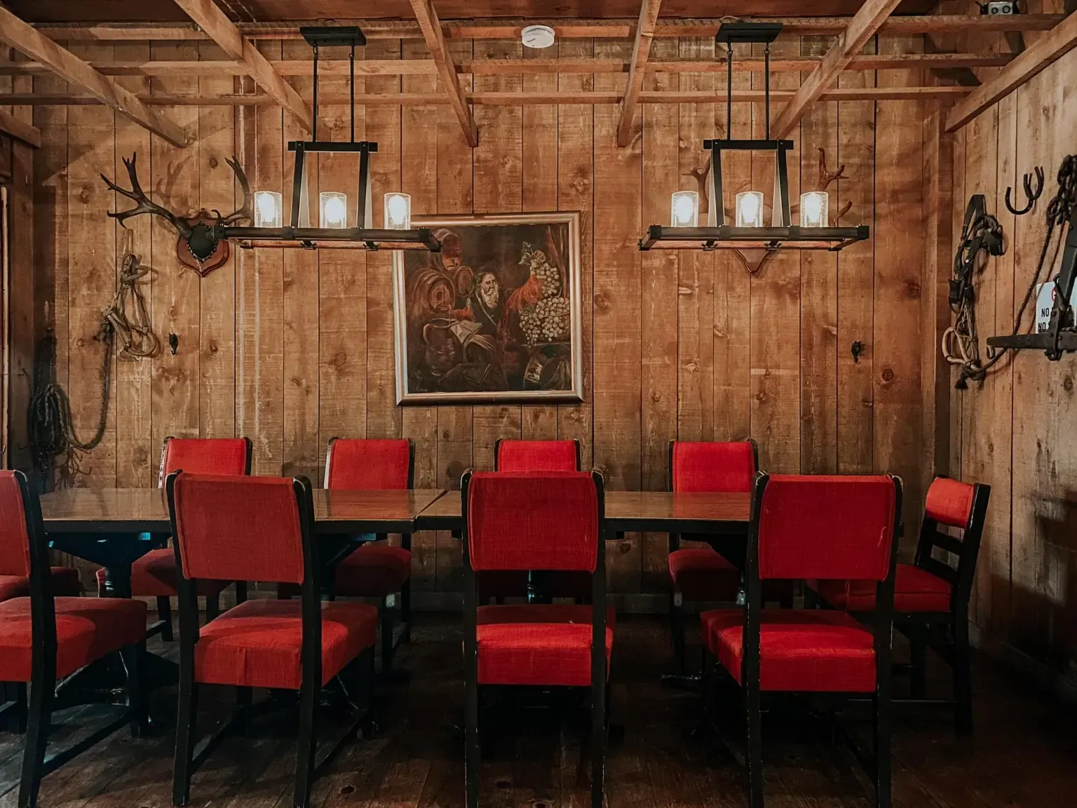 Comedor con paredes de madera, sillas rojas y una mesa larga. Dos lámparas de araña cuelgan del techo.