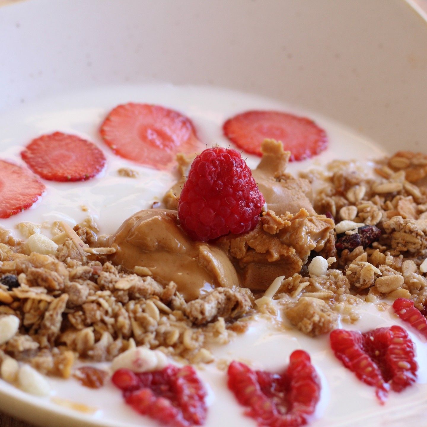 Tazón de yogur con granola, mantequilla de cacahuete, fresas en rodajas y frambuesas.