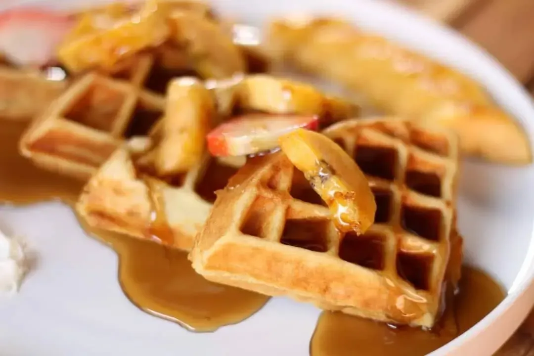 Gofres con manzanas glaseadas con caramelo y sirope en un plato blanco.