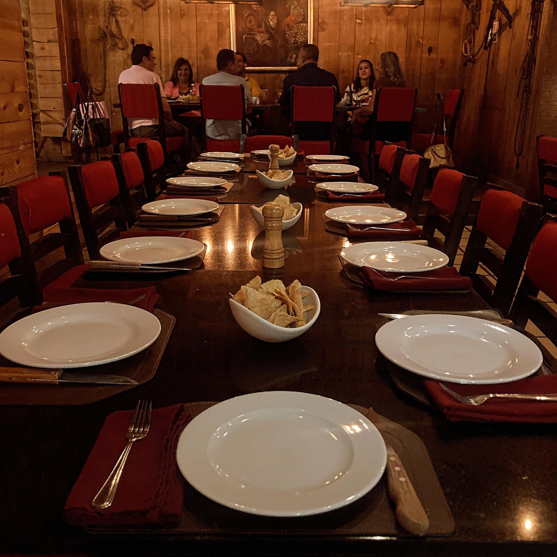 Mesa de comedor larga puesta para una comida en un restaurante con gente sentada al fondo.