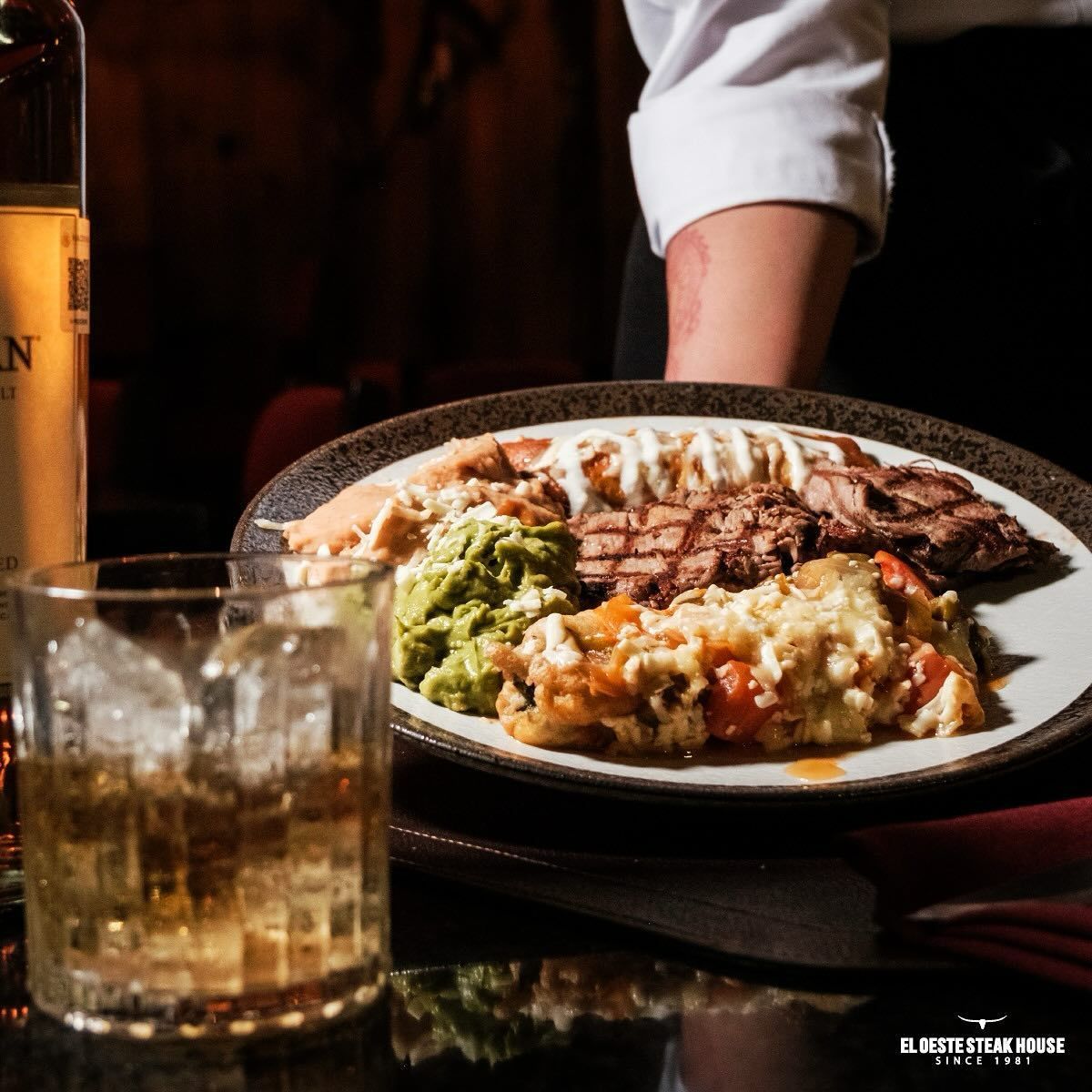 Plato de comida servido con un vaso de líquido ámbar y hielo.