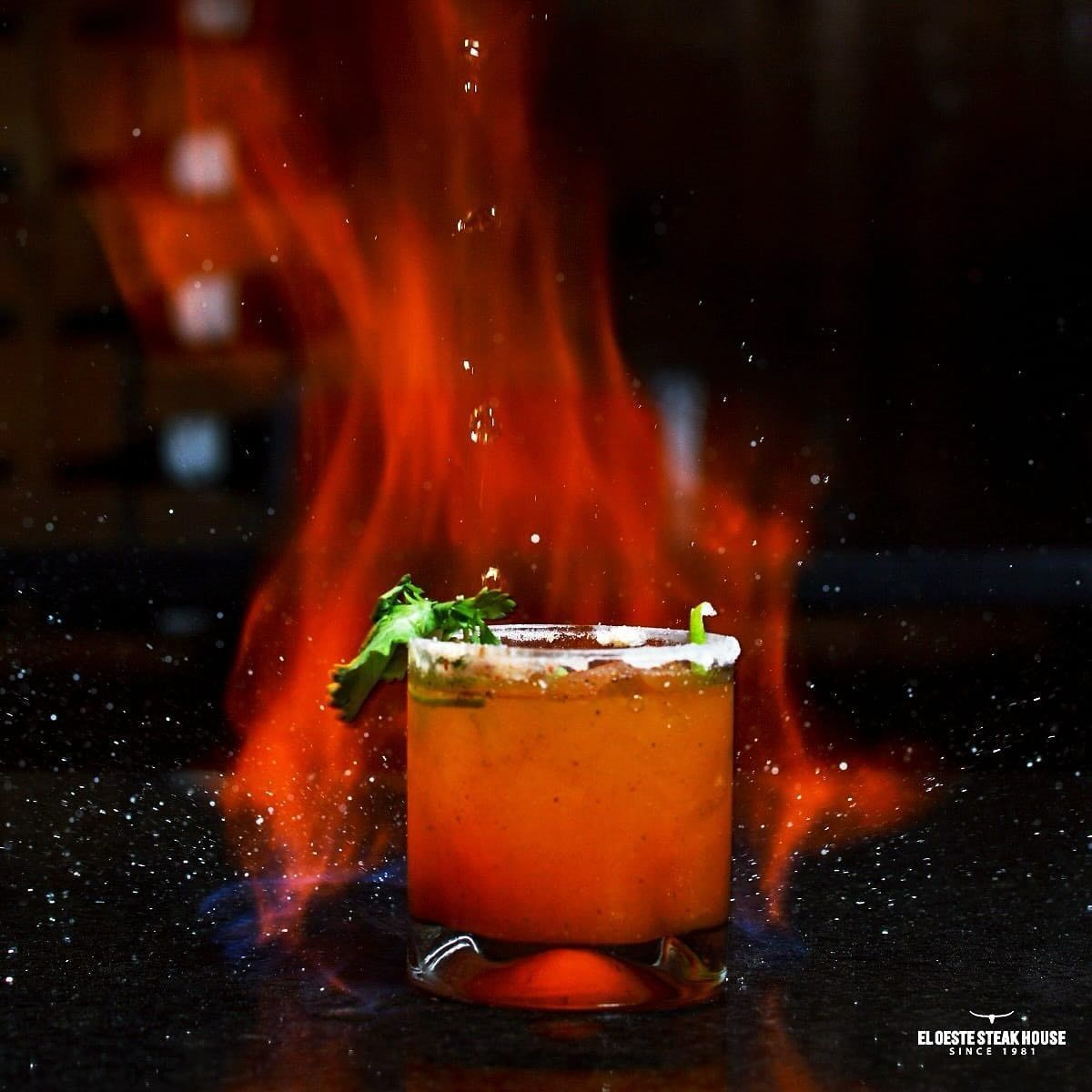 Copa de cóctel llameante con borde de sal, rodeada de llamas.