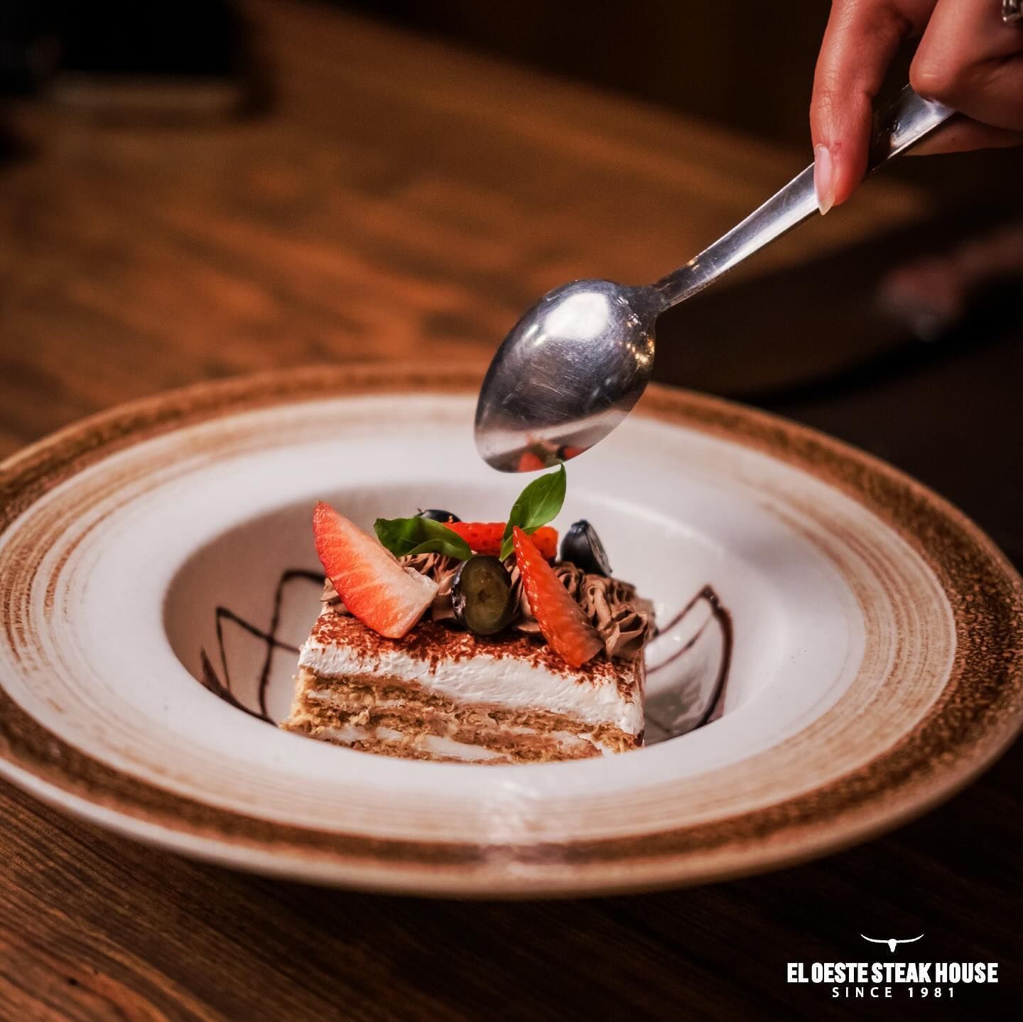 Postre bañado en salsa en un plato con fresas, arándanos y chocolate.