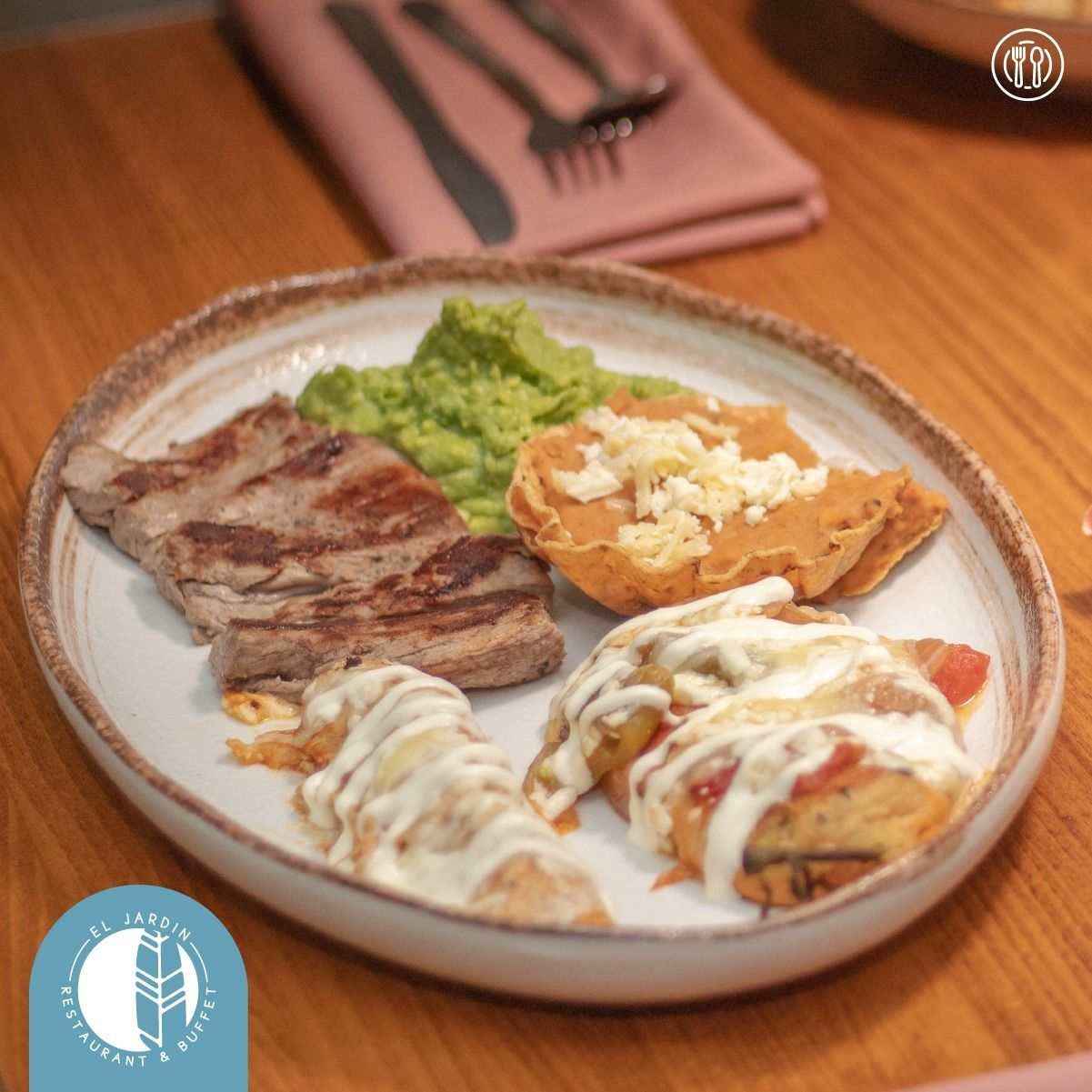 Plato con filete a la parrilla, puré de aguacate, patata rellena y otros dos platos, con cubiertos al fondo.