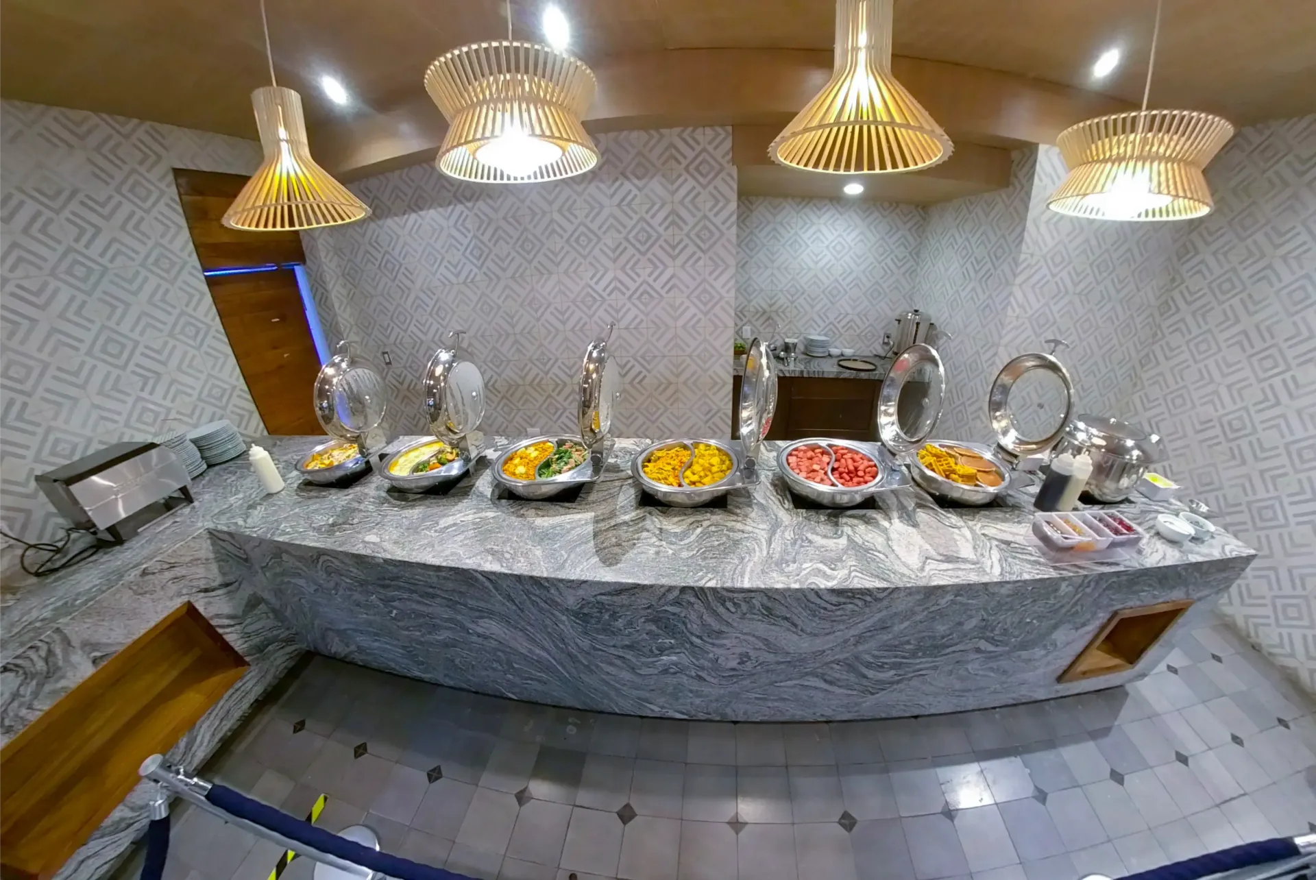 Buffet con diversos alimentos sobre una encimera bajo iluminación decorativa.