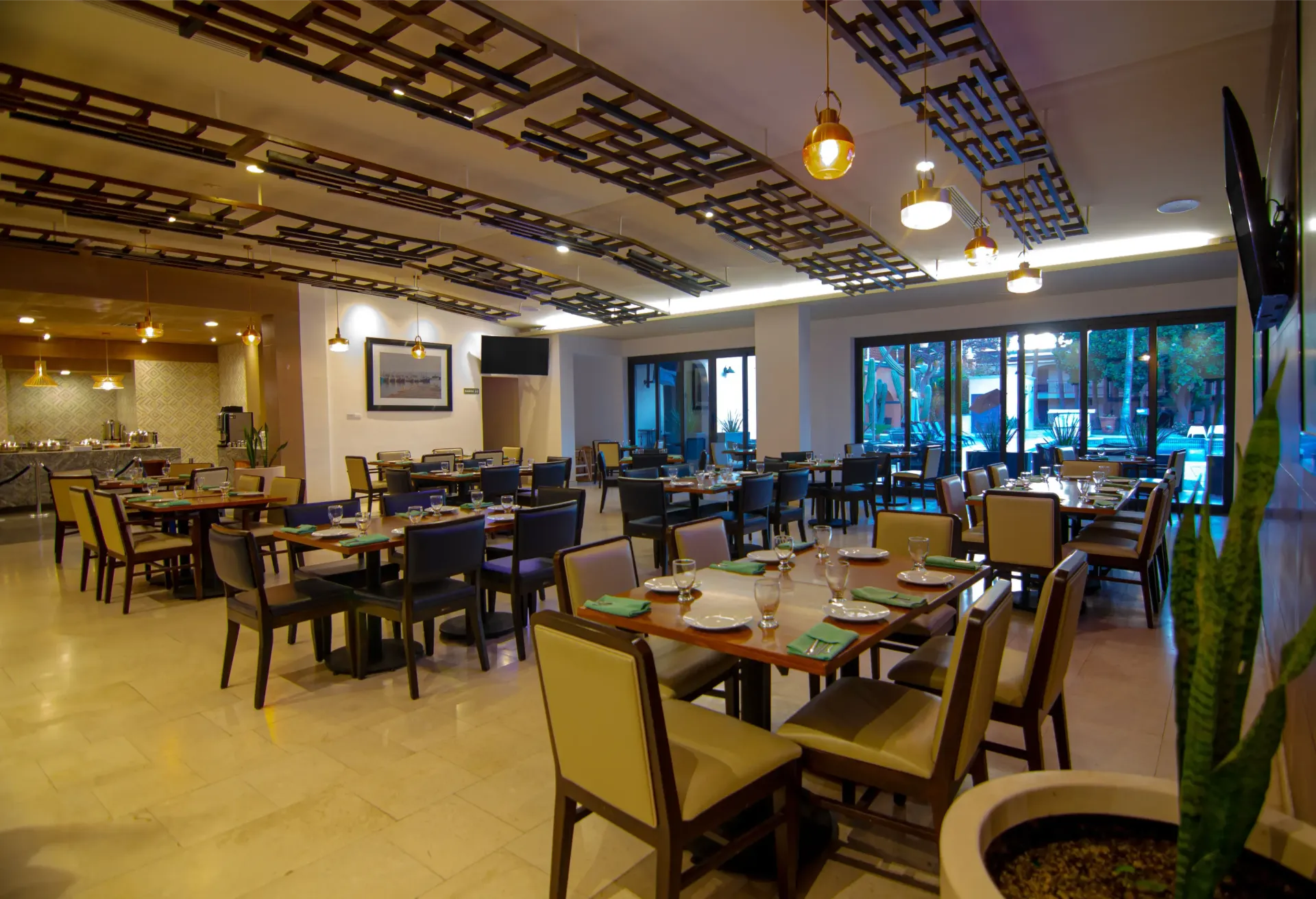 Interior de restaurante con mesas, sillas y grandes ventanales. Colores neutros y paneles decorativos en el techo.