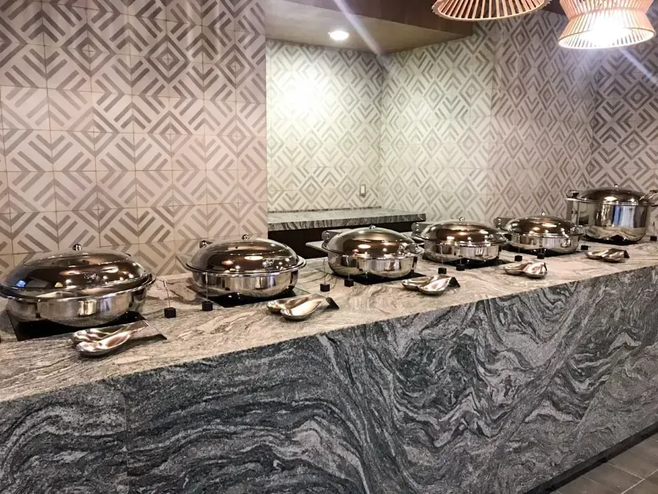 Aparador con vajilla de plata sobre encimera de granito, pared de azulejos estampados, bajo iluminación cálida.