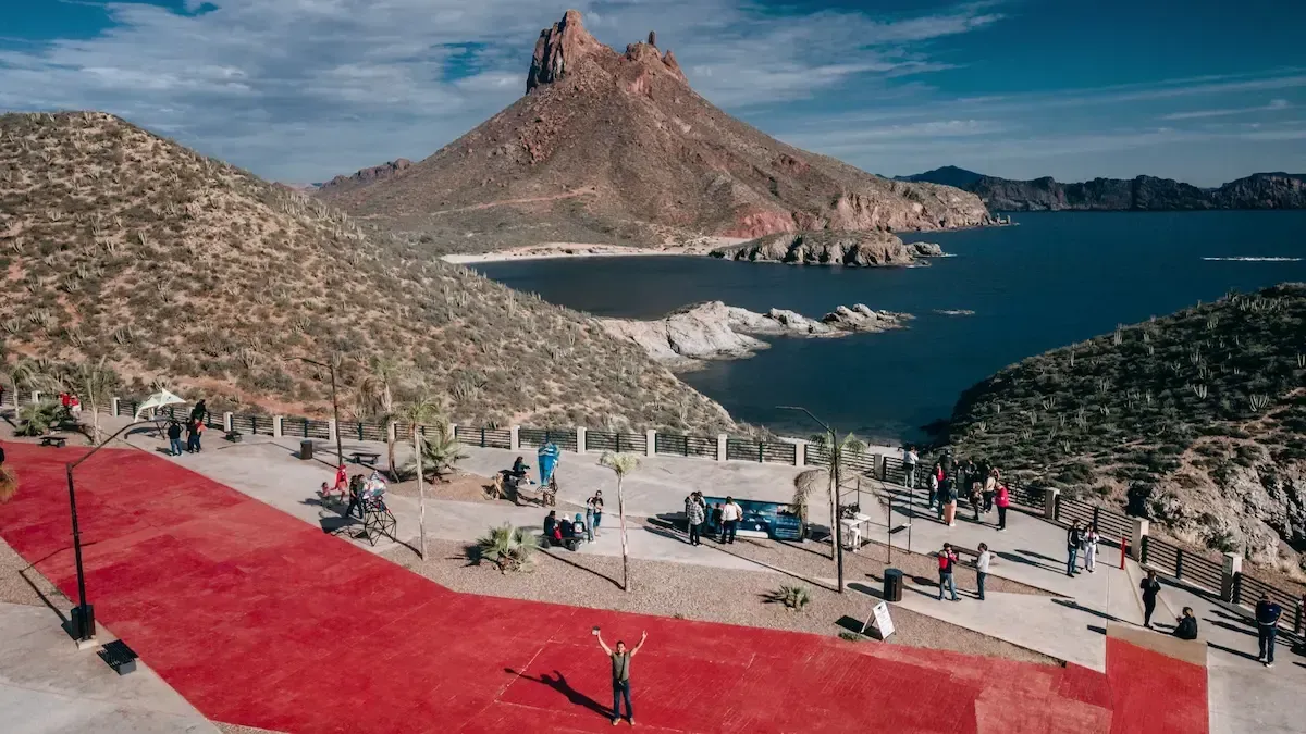 Sunset over a city skyline with water in the foreground, fiery orange sky, silhouetted buildings.