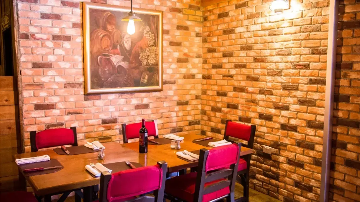 Un comedor con una mesa de madera, sillas rojas, paredes de ladrillo y un cuadro.