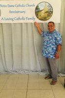 Person pointing at a Notre Dame Catholic Church anniversary banner beside a gray curtain.