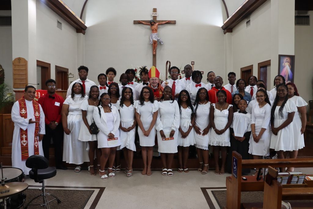 Group of people in white and red robes posing in a church before a crucifix.