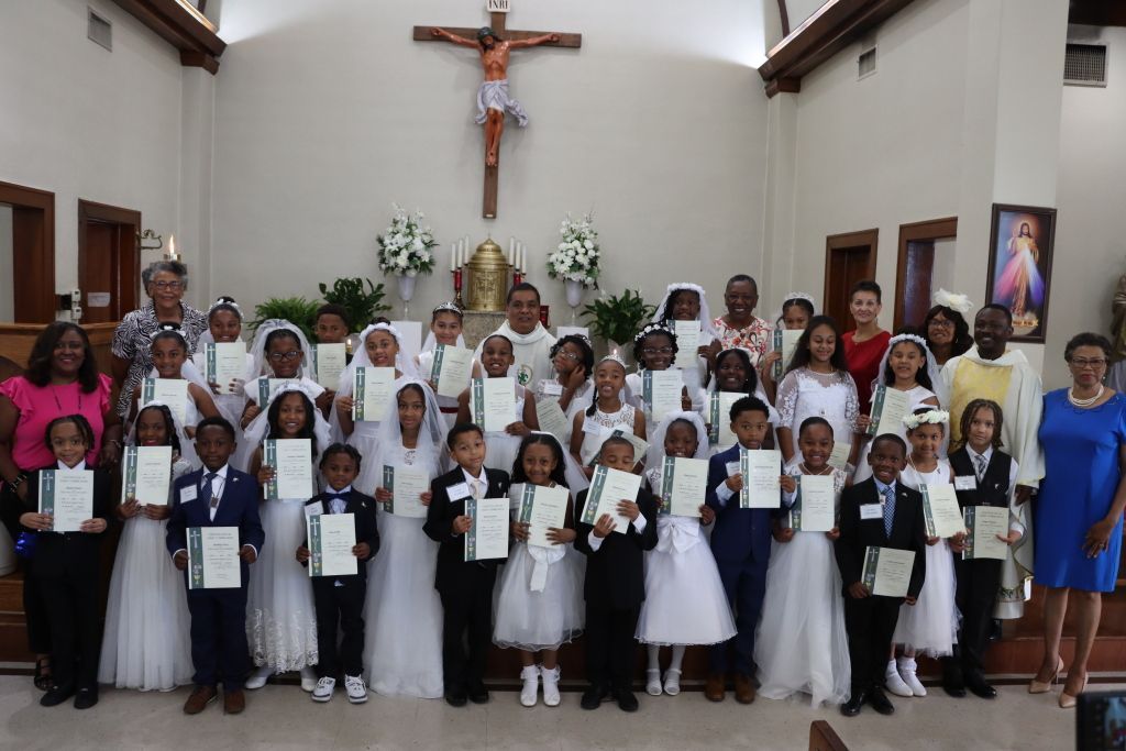 Group of children and adults in white clothing posing inside a church beneath a crucifix.