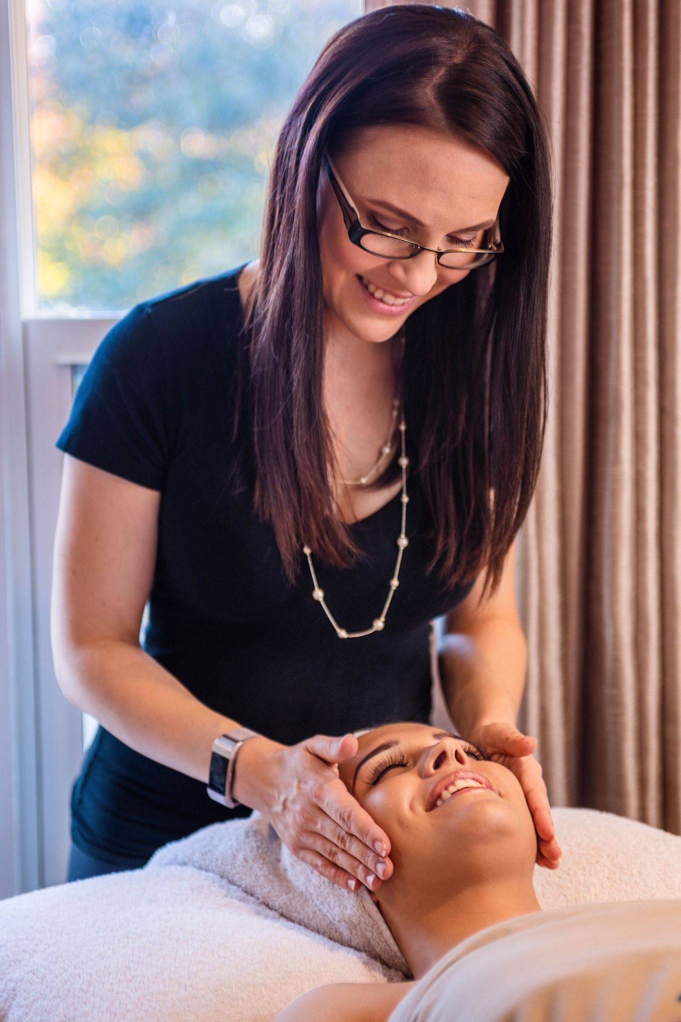 Woman in glasses giving a facial to a person lying on a massage table.