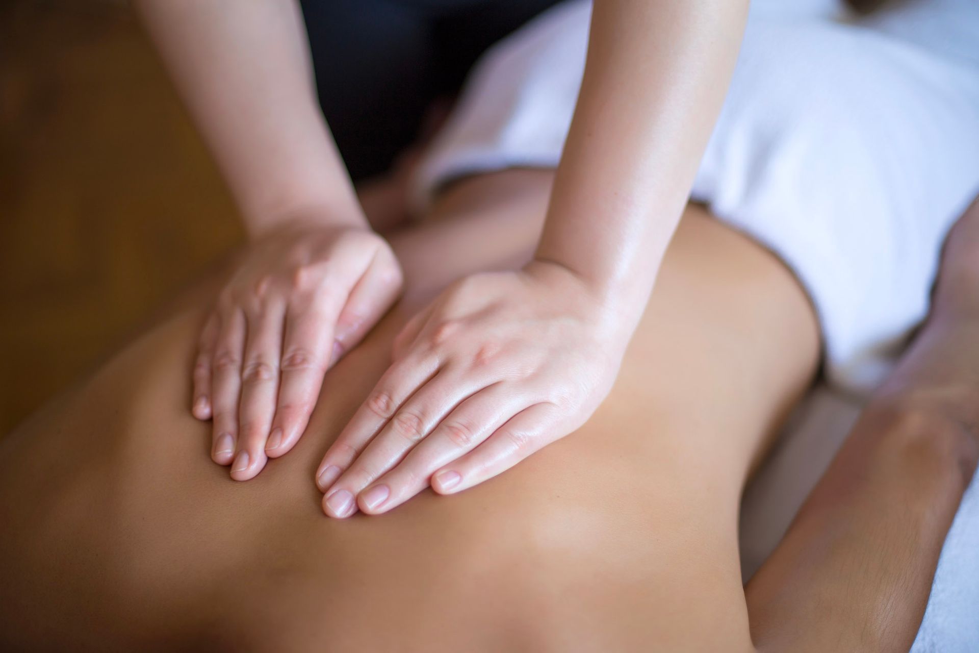 Hands massaging a person's back, on a massage table covered in a white sheet.