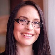 Woman with dark hair wearing glasses smiling.