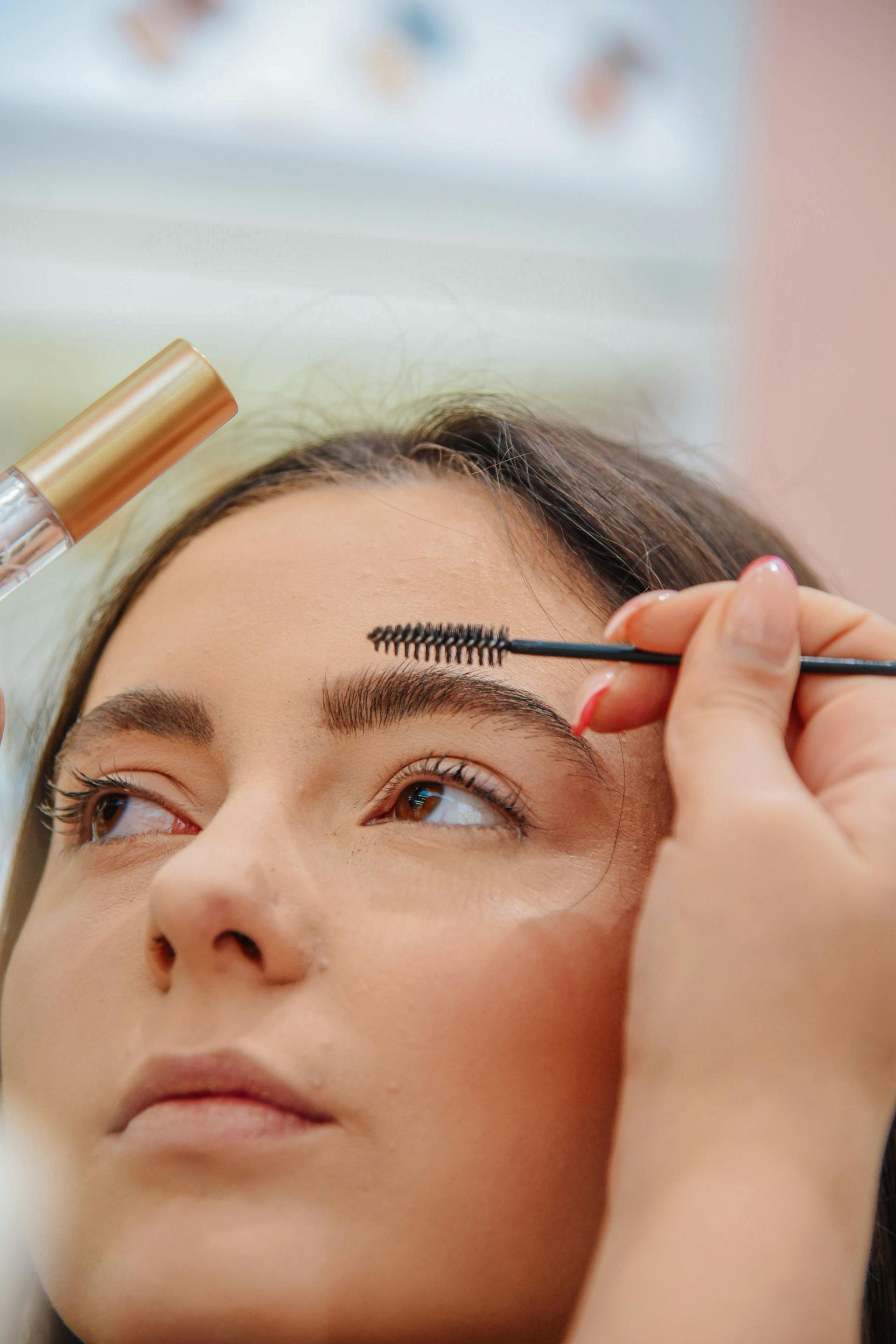 Person having eyebrow makeup applied with a brush. Gold tube of product visible.