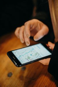 Person using smartphone, navigating map app on a wooden table.
