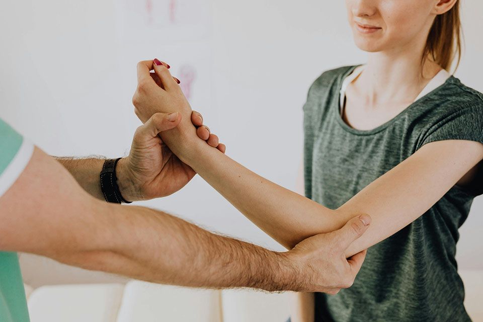 A person's arm being examined by a healthcare professional. Elbow bent, neutral expression. White room.