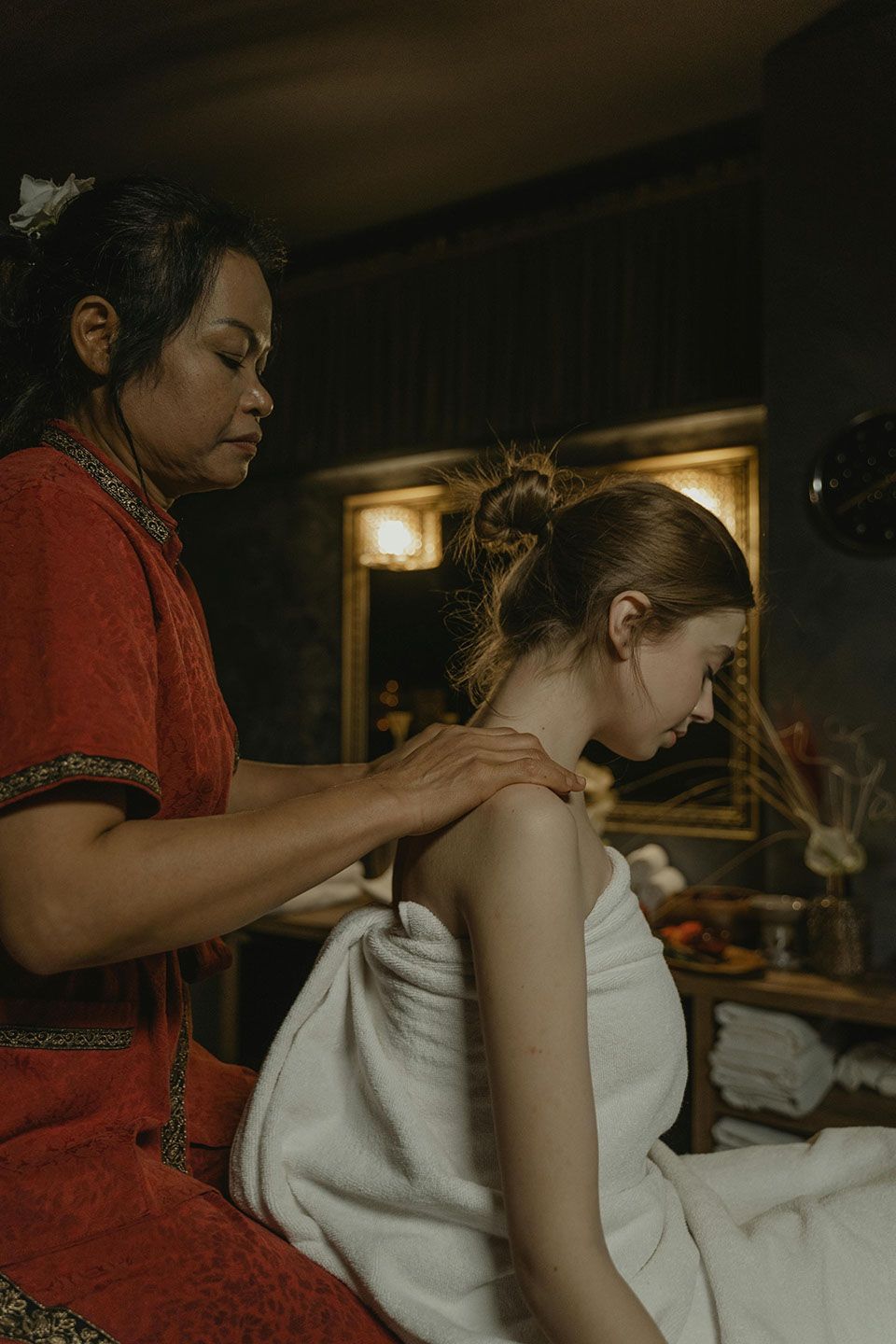 Woman receiving shoulder massage in dimly lit room.