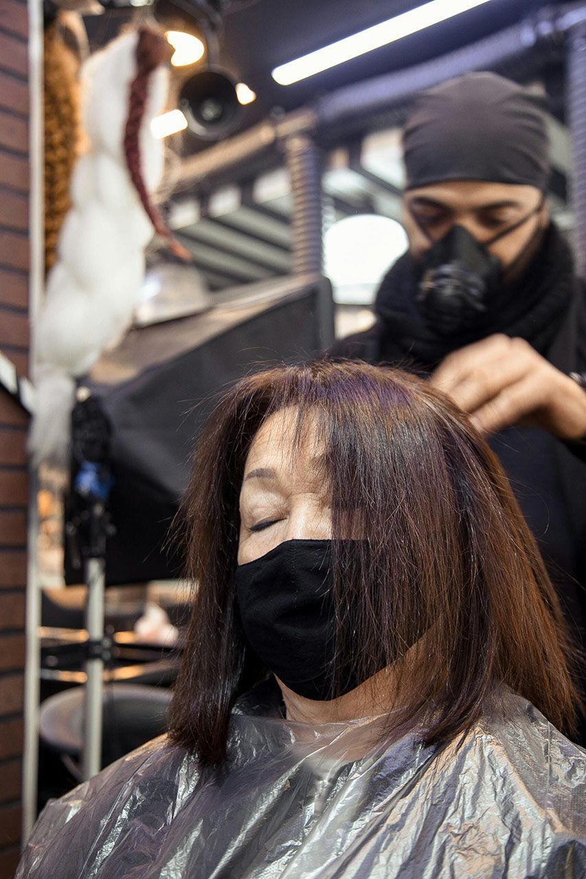 Person getting their hair styled by someone wearing a mask, inside a salon.
