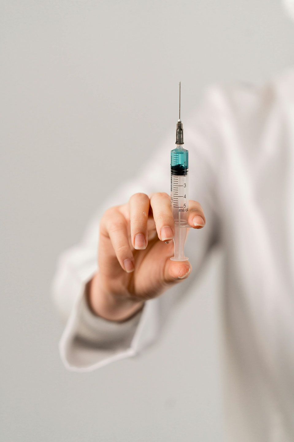 Person holding a syringe filled with blue liquid, ready to administer an injection.