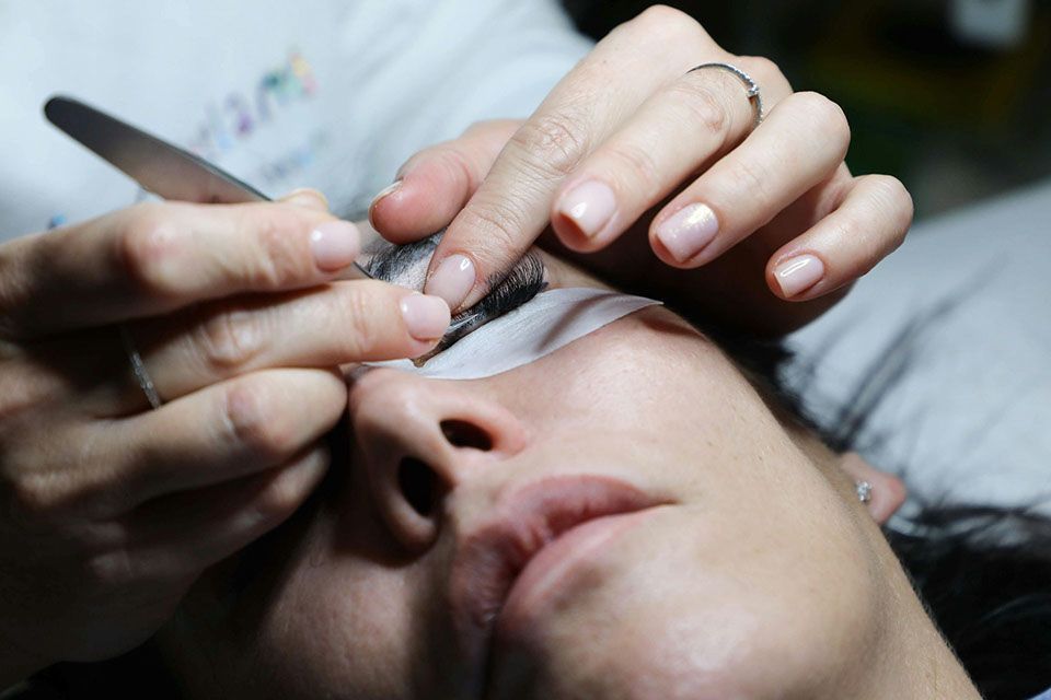 Person receiving eyelash extensions. Technician uses tweezers, close up.
