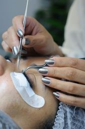 Person getting eyelash extensions applied with tweezers.